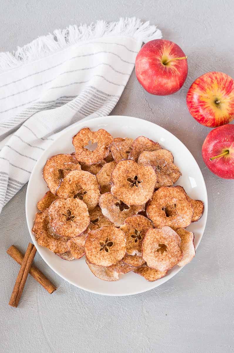 baked apple chips in a white plate and red apples