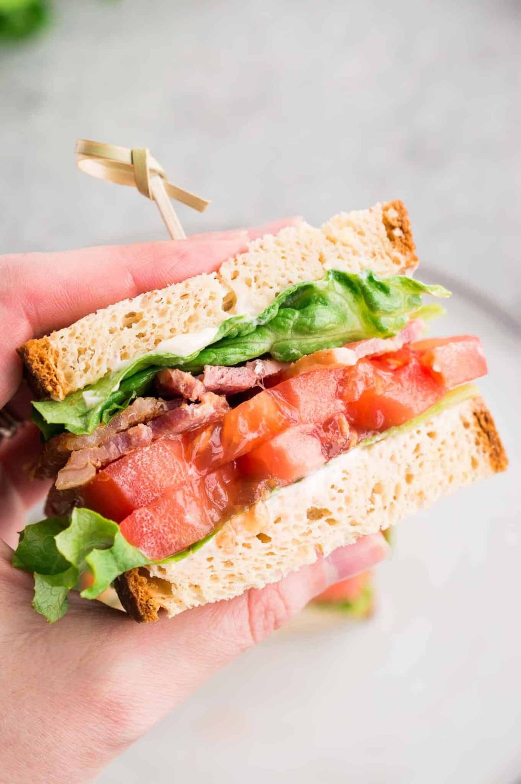 holding sliced tomato bacon sandwich