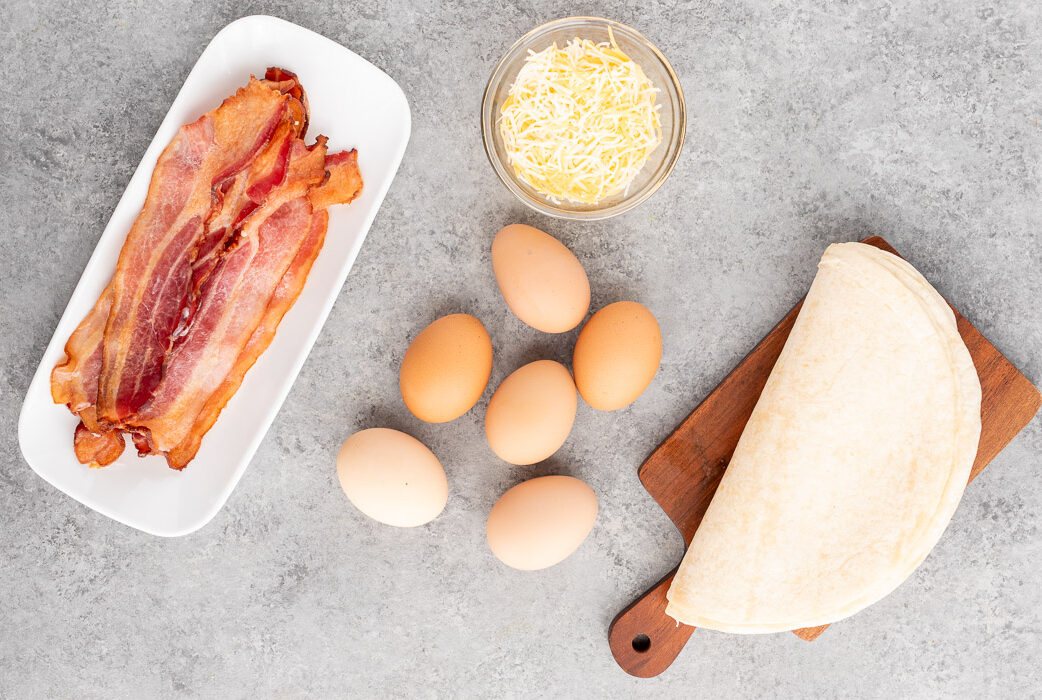 eggs, cheese, bacon and tortillas on a board