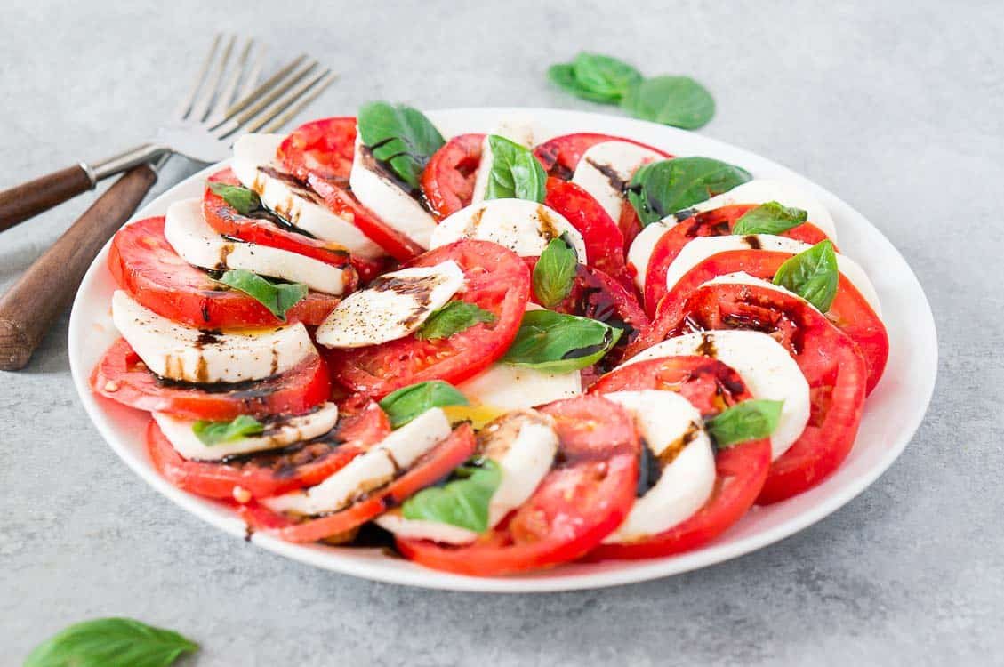 layered caprese salad on a white plate and gray board