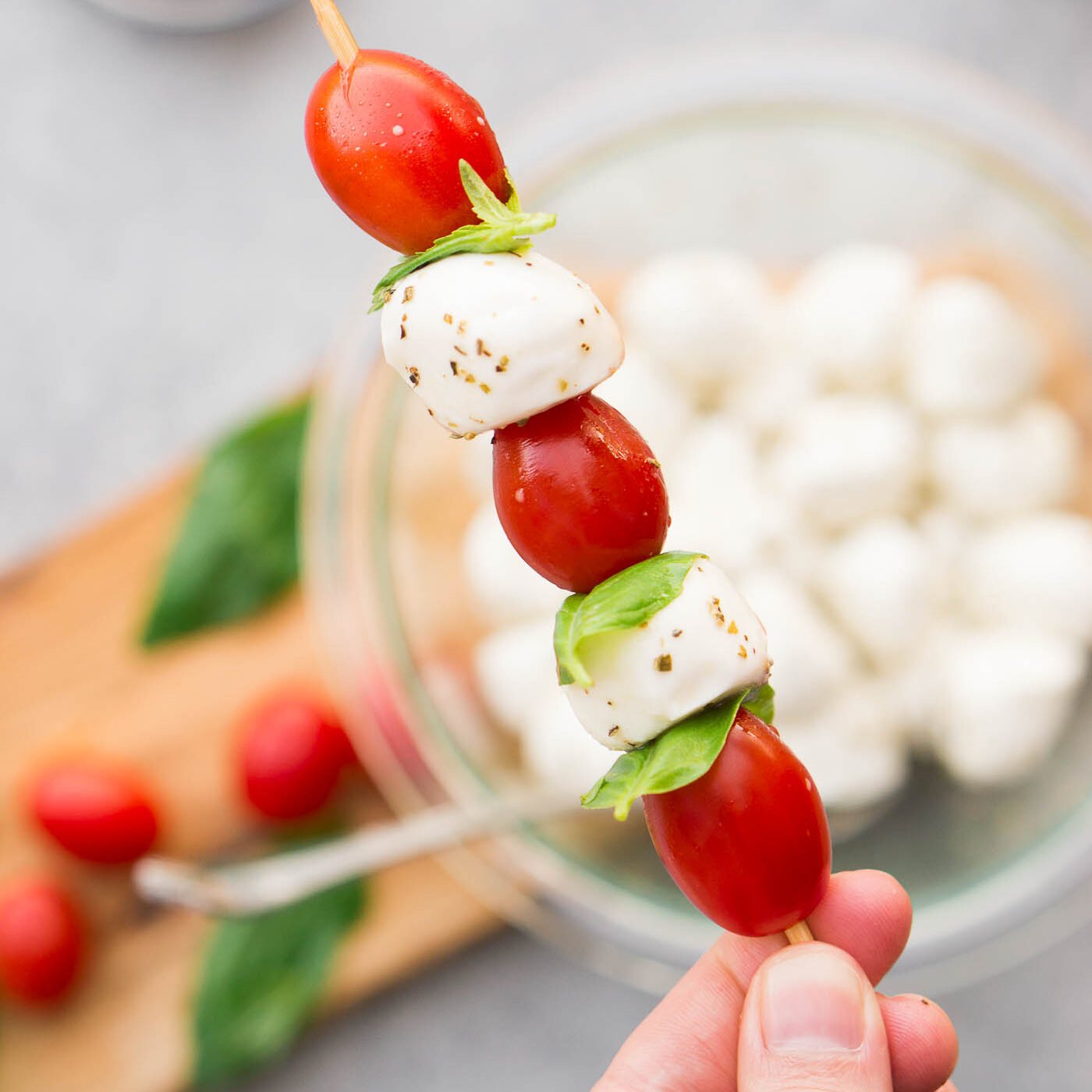 threading mozzarella balls tomatoes and basil leaves on skewers
