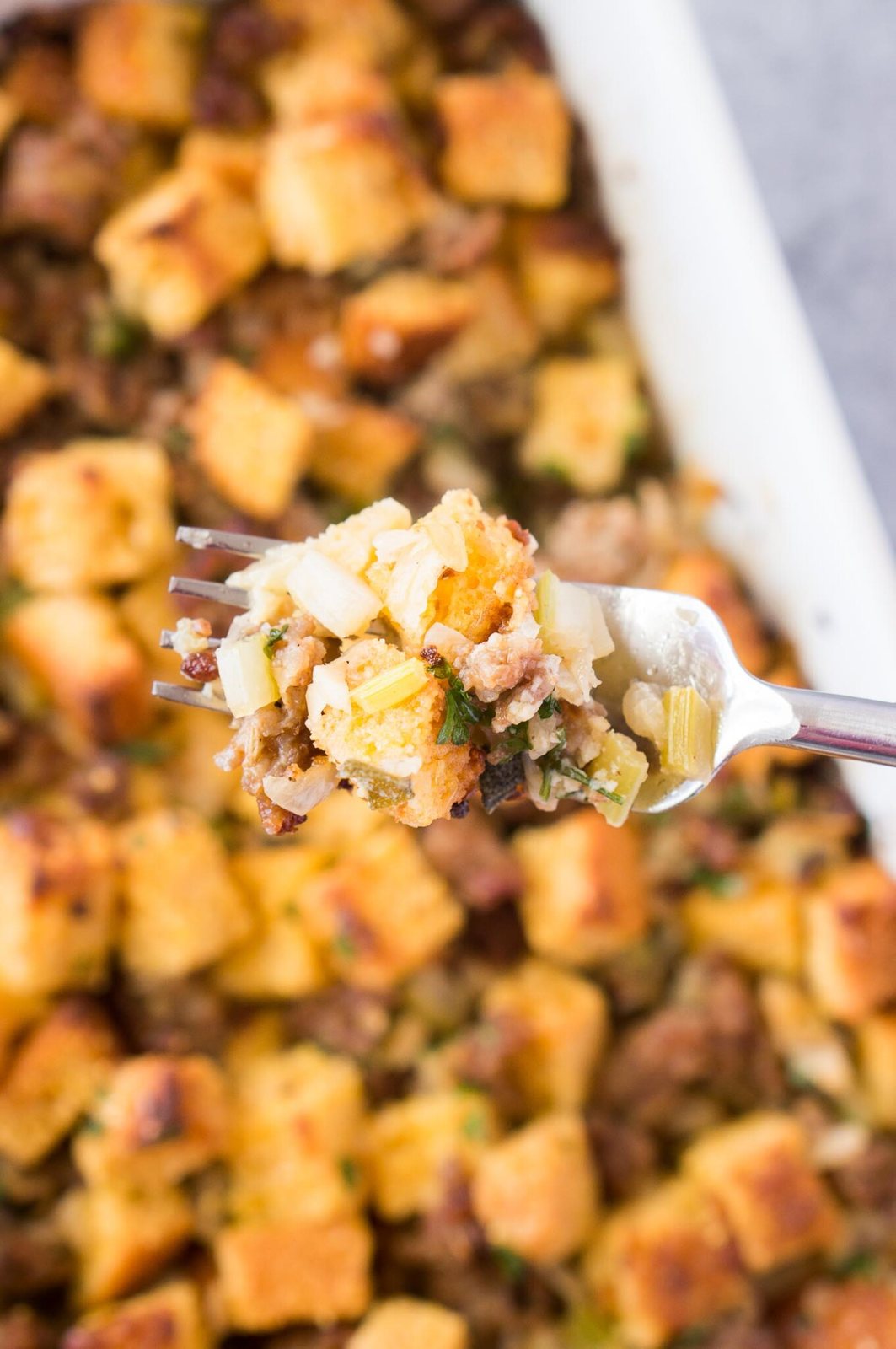 taking a spoonful of sausage and cornbread dressing in a casserole dish