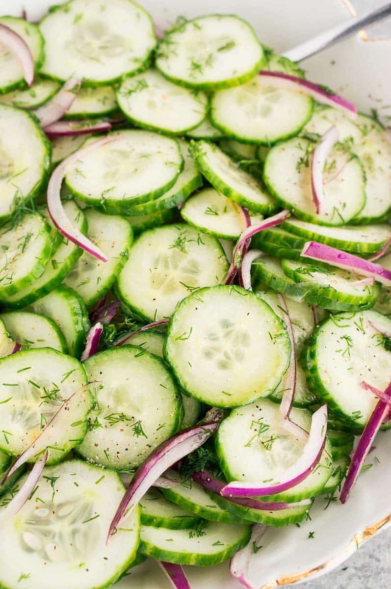 cucumber slices, red onion, dill, and dressing in a white bowl