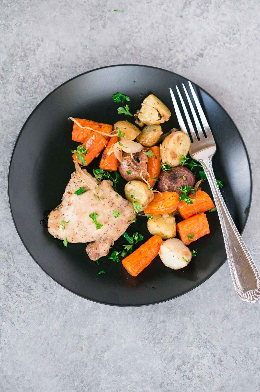 Baked Chicken and Potatoes on a black plate with a fork