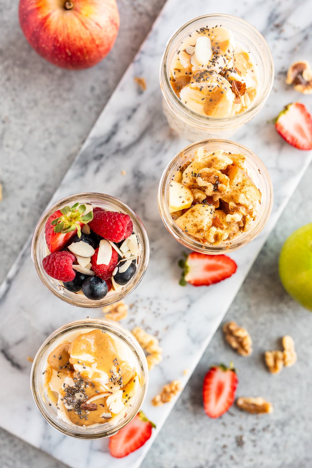 Overhead view of overnight oats jars with different toppings including berries, apple cinnamon, walnuts, and peanut butter, perfect for meal prep breakfast ideas.
