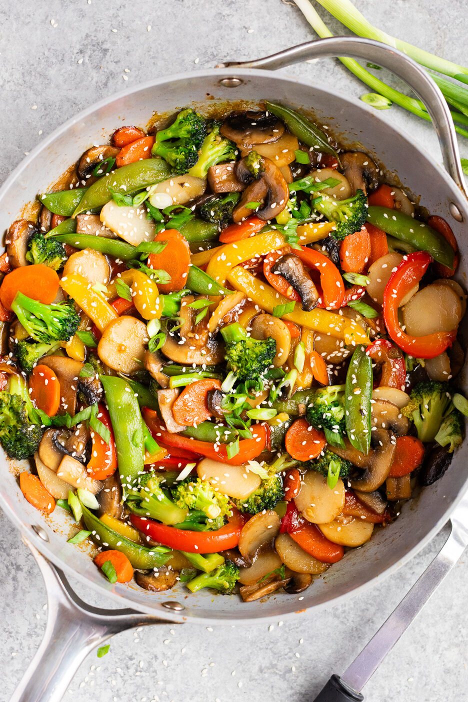 Finished weeknight vegetable stir fry garnished with green onions and sesame seeds, served straight from the skillet