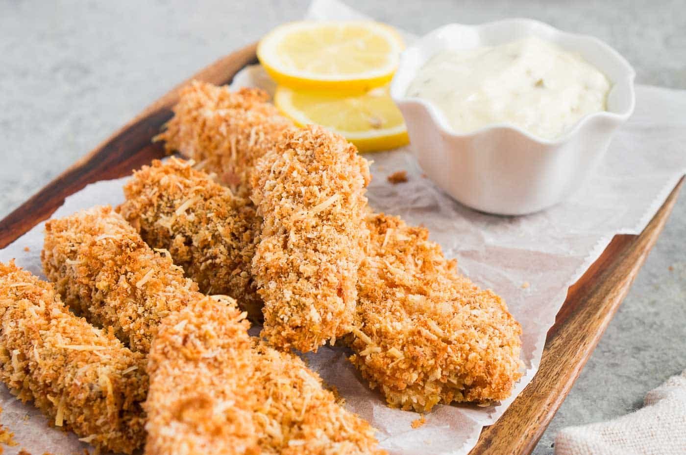 close of fish fingers on a board and tartar sauce
