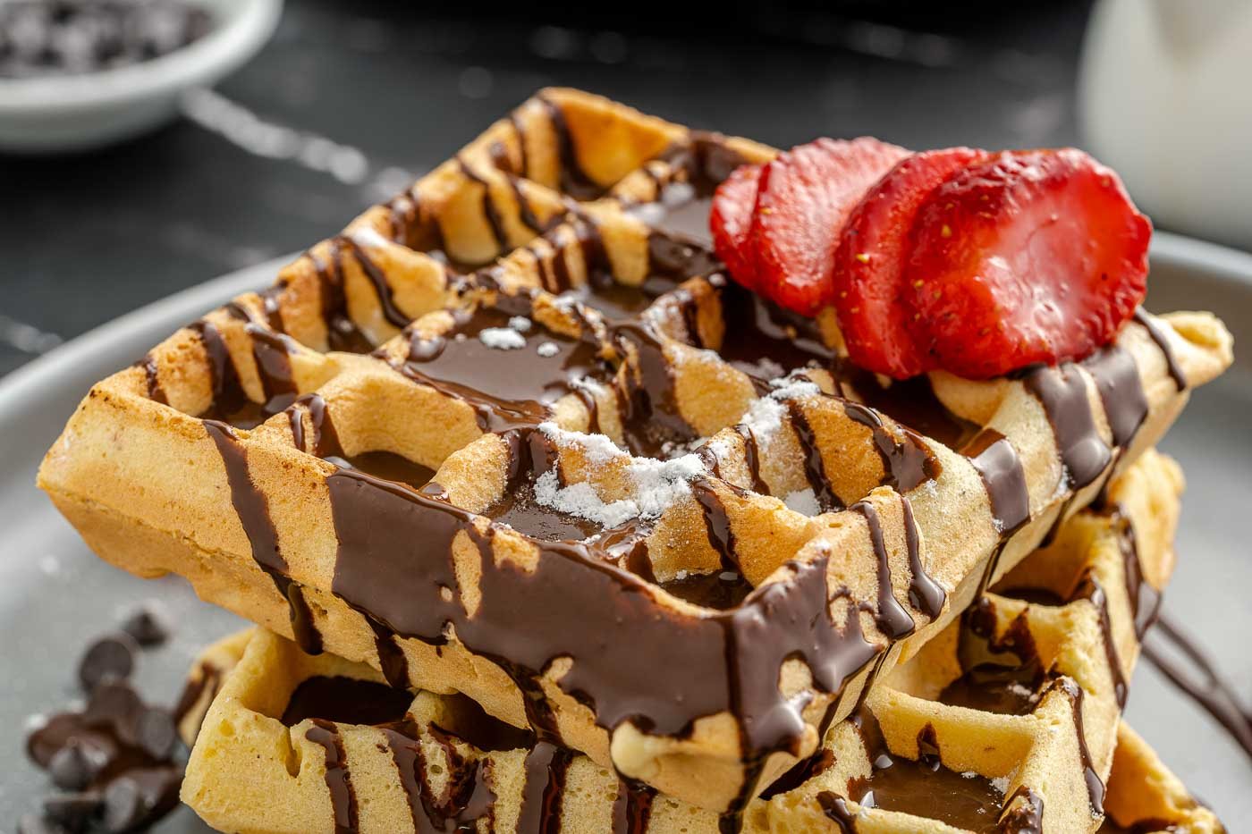 waffles on a plate drizzled with chocolate and topped with sliced strawberry
