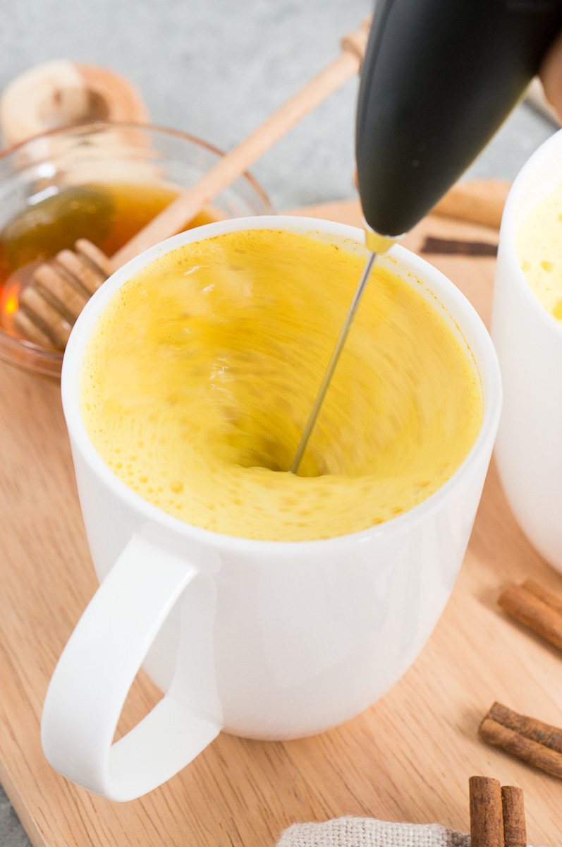 mixing turmeric and other spices with milk in a mug