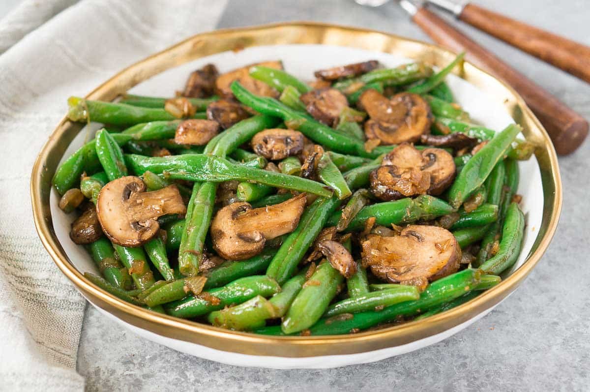 healthy green beans and mushrooms on a board with fork and napkin in background