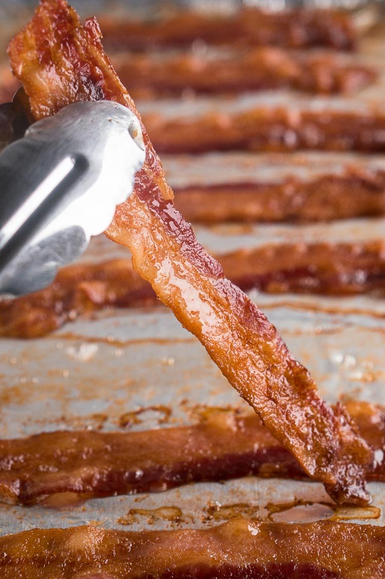 holding oven baked bacon slice with tongs