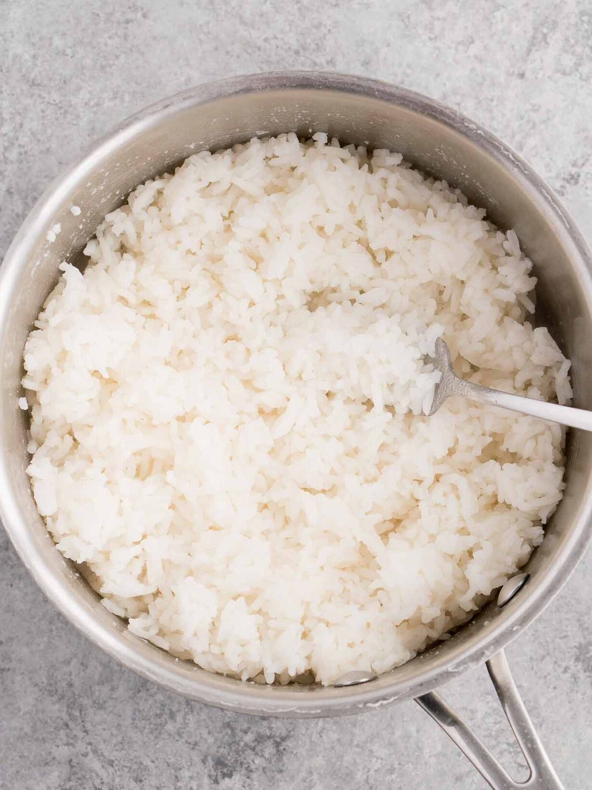 fluffing cooked white rice with a fork in a pot