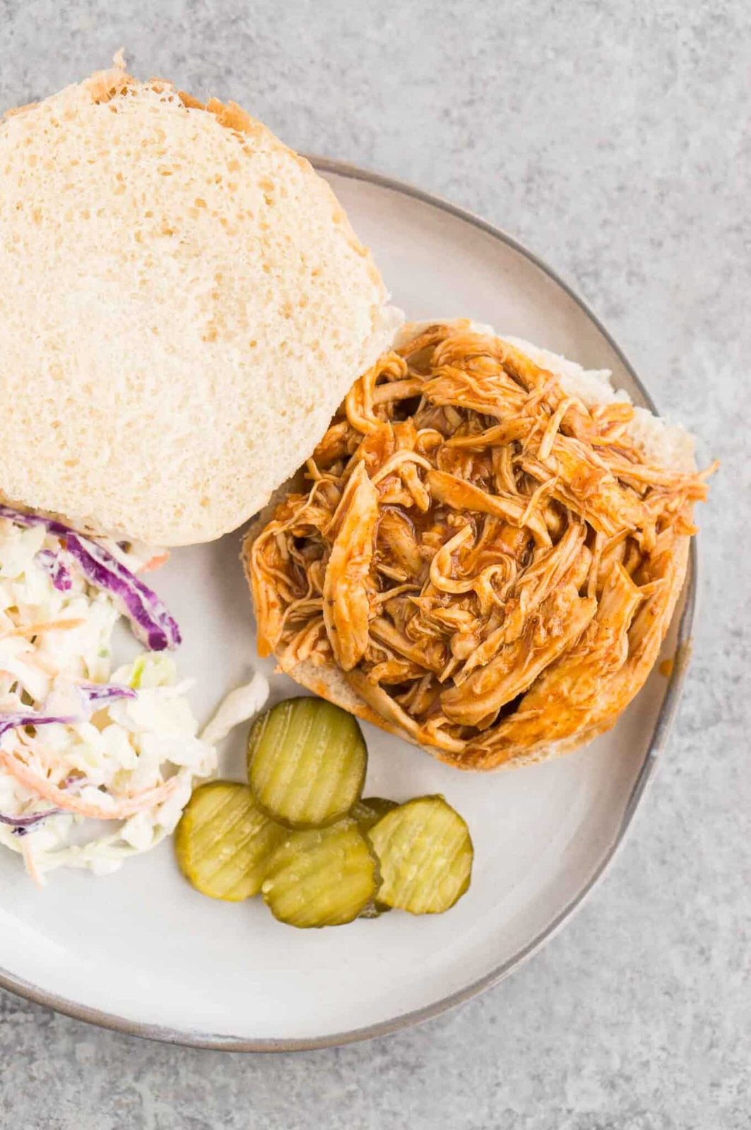 pulled bbq chicken on a bun with pickles and coleslaw