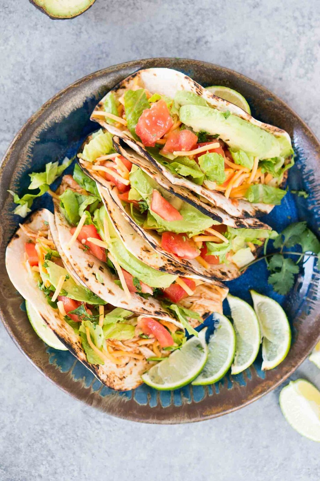 chicken tacos with lettuce, tomatoes, avocado and cheese on a plate