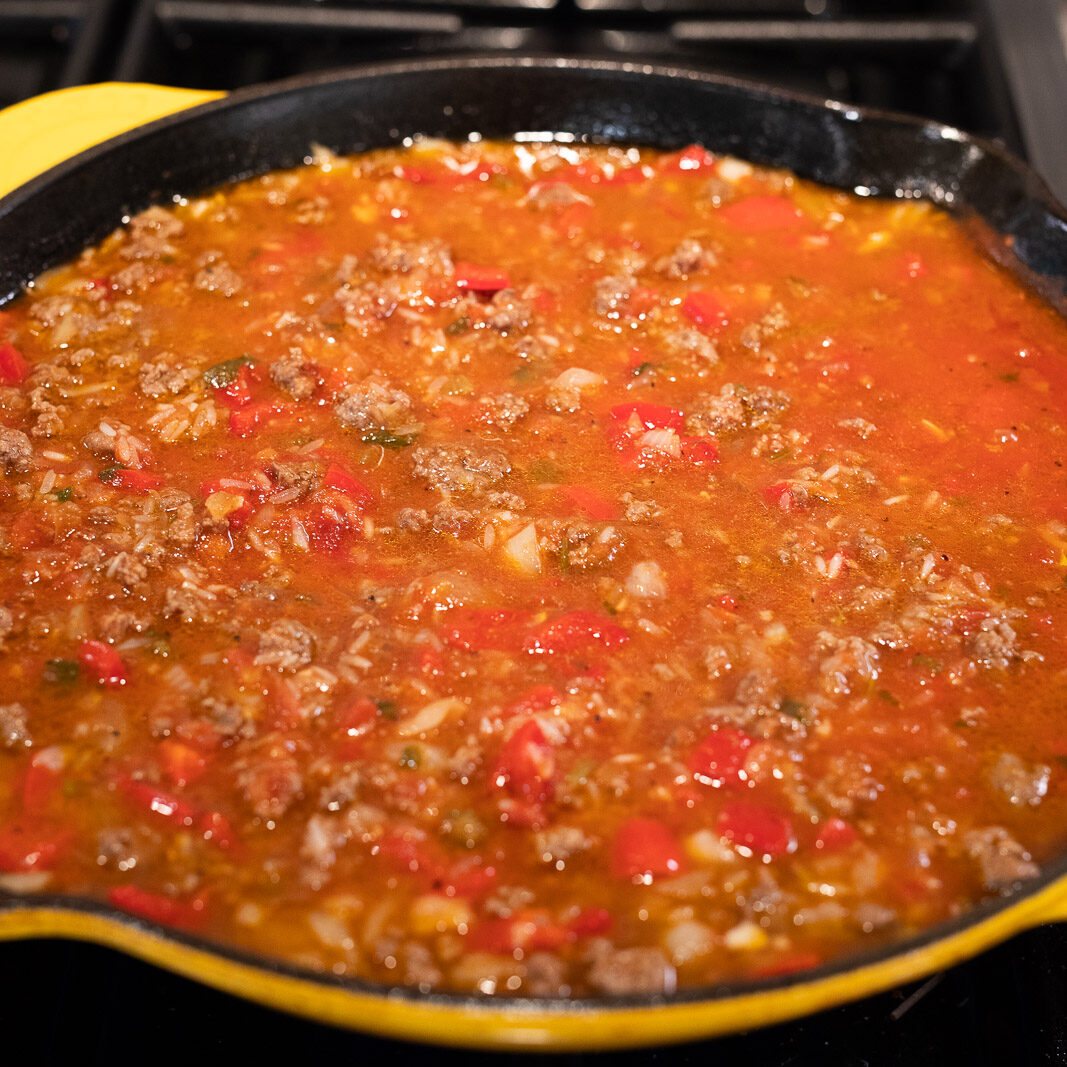 cooking rice, salsa, tomato sauce with beef and vegetables in a skillet