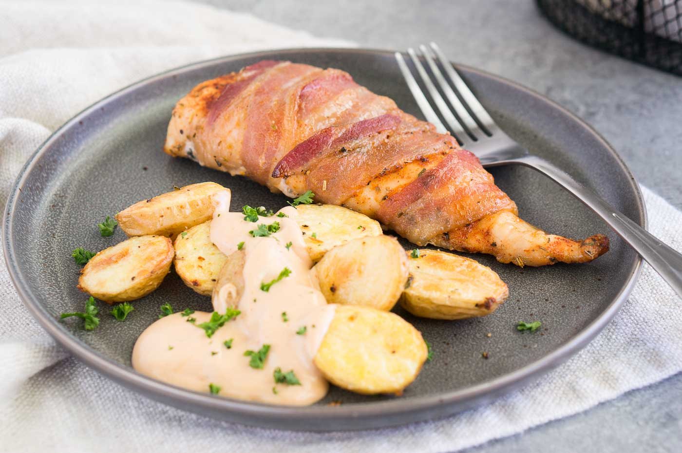 close up image of chicken wrapped in bacon with roasted potatoes on a plate