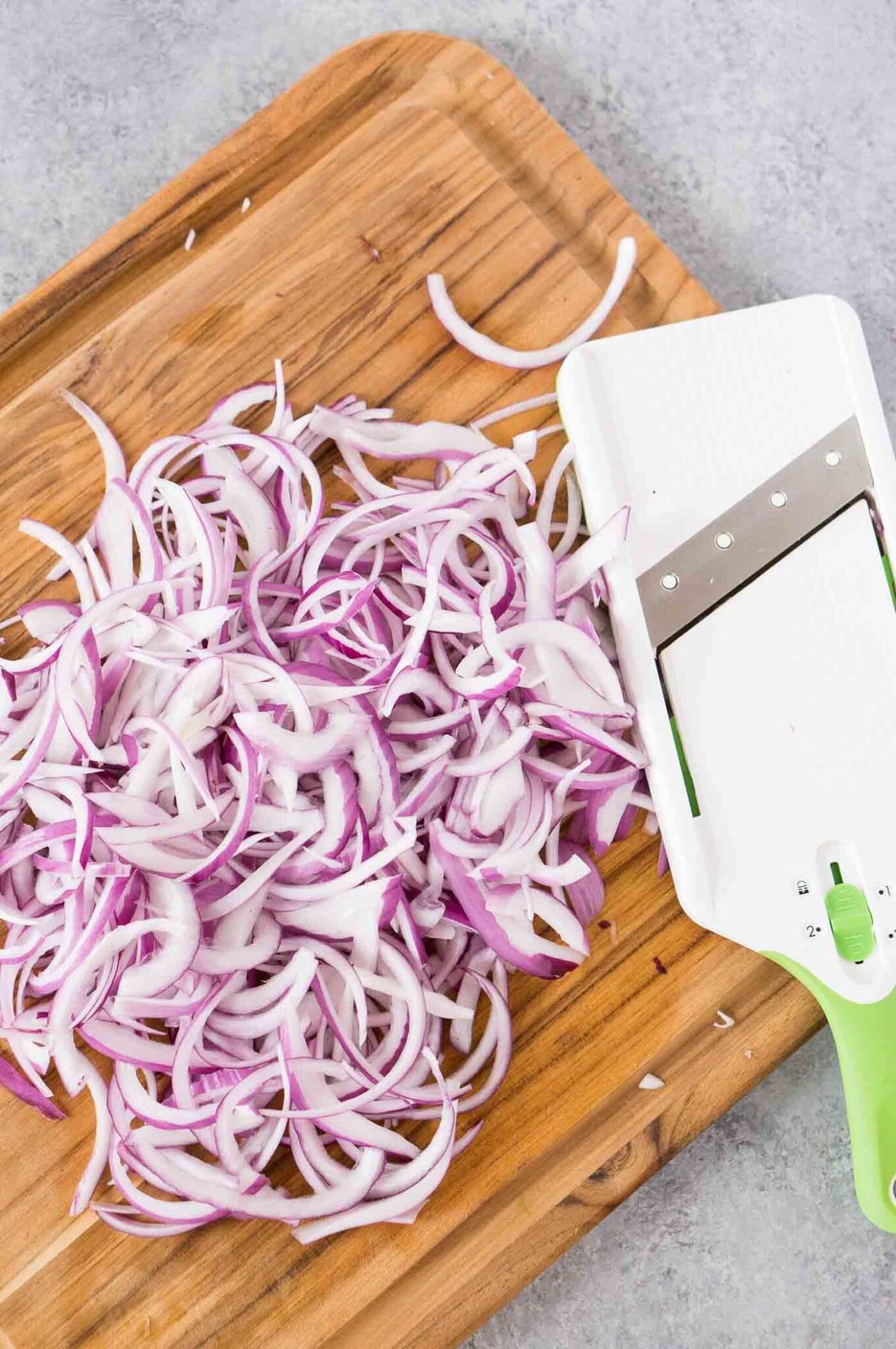 thinly sliced red onion with mandolin on a cutting board