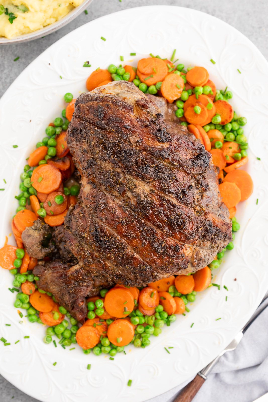 Roasted lamb recipe with garlic and herbs rub served with carrots and peas