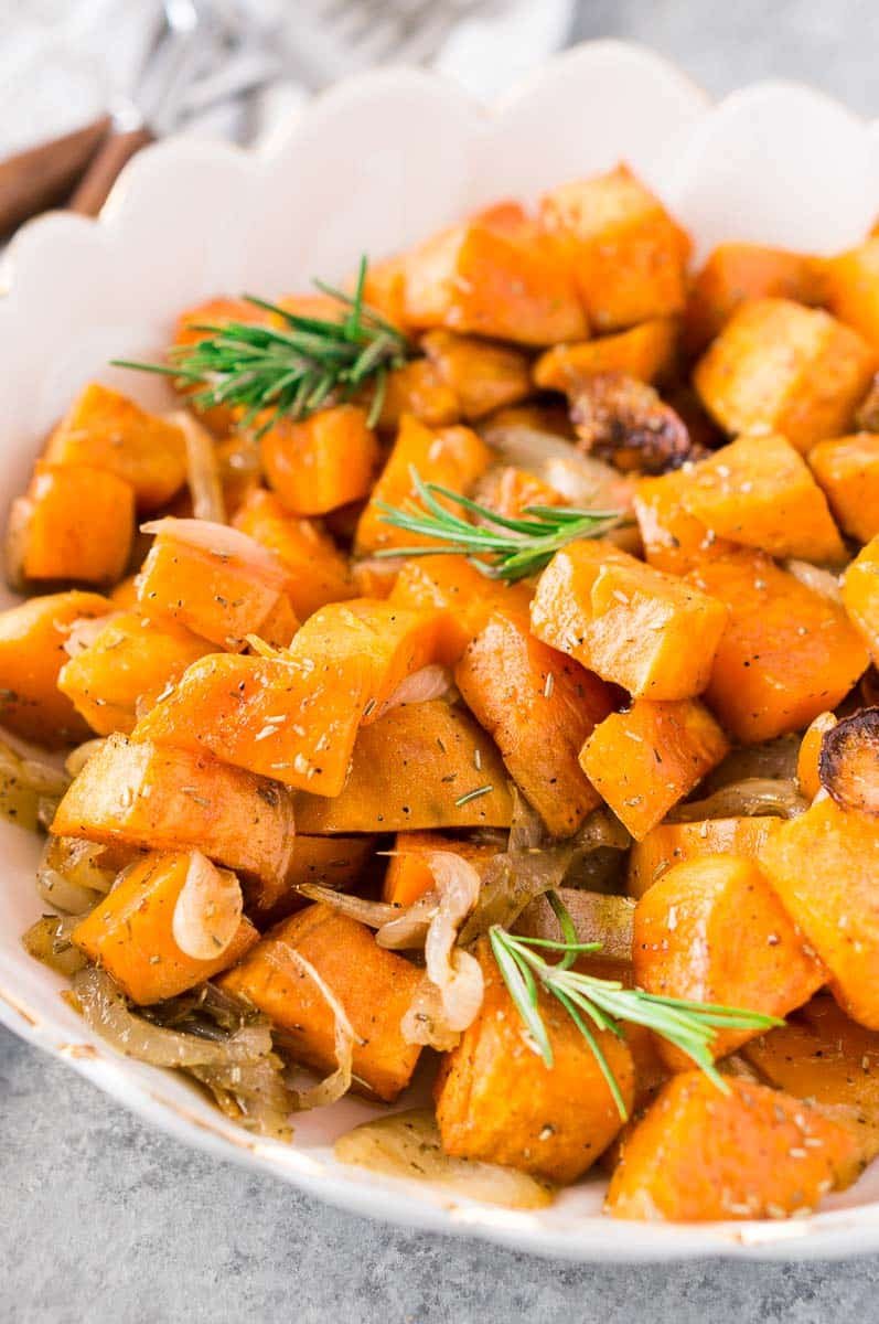 close up shot of sweet potatoes and onions served in a white bowl
