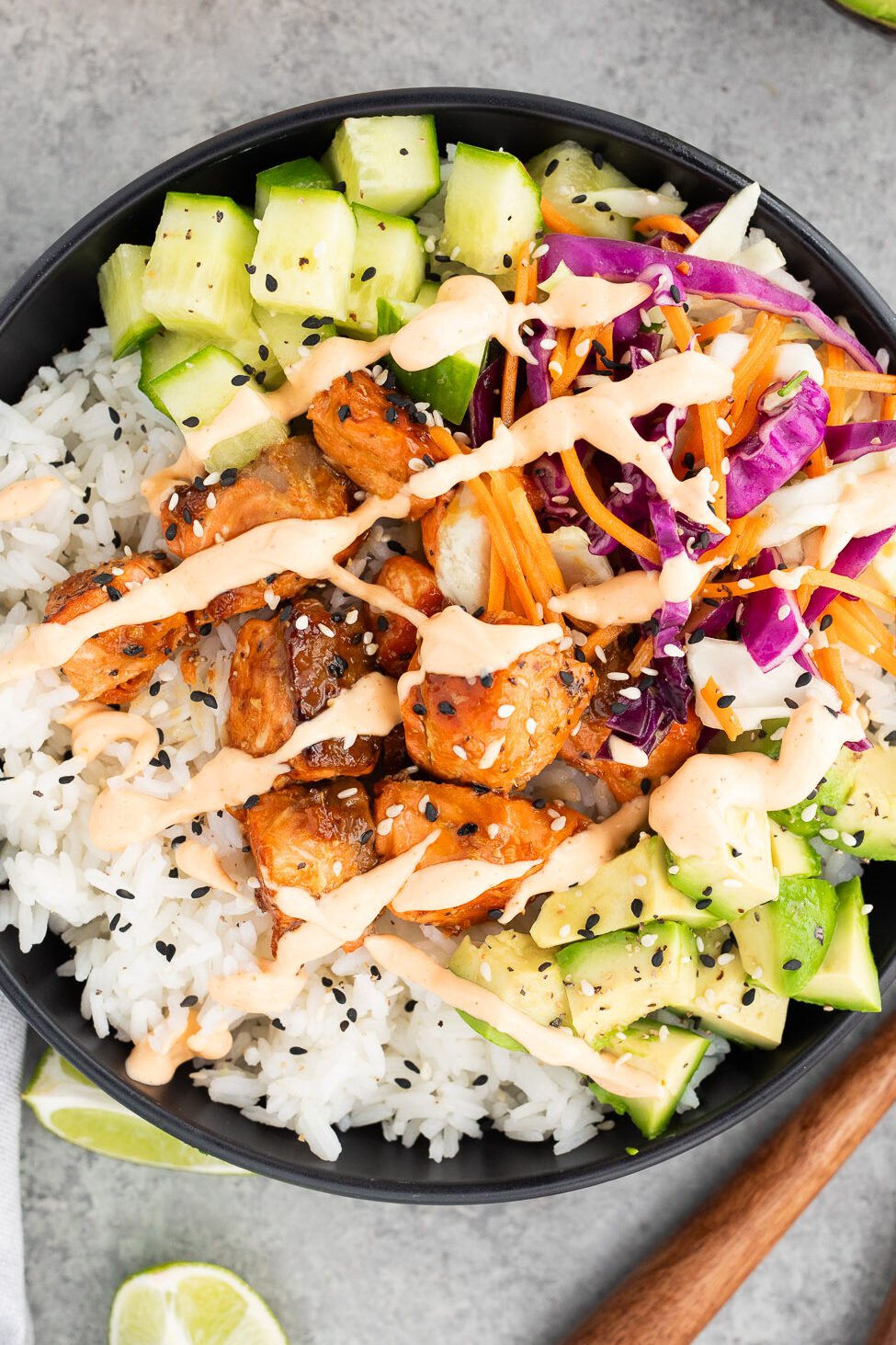 salmon served in a bowl over rice with cucumbers, avocados, slaw and sriracha mayo