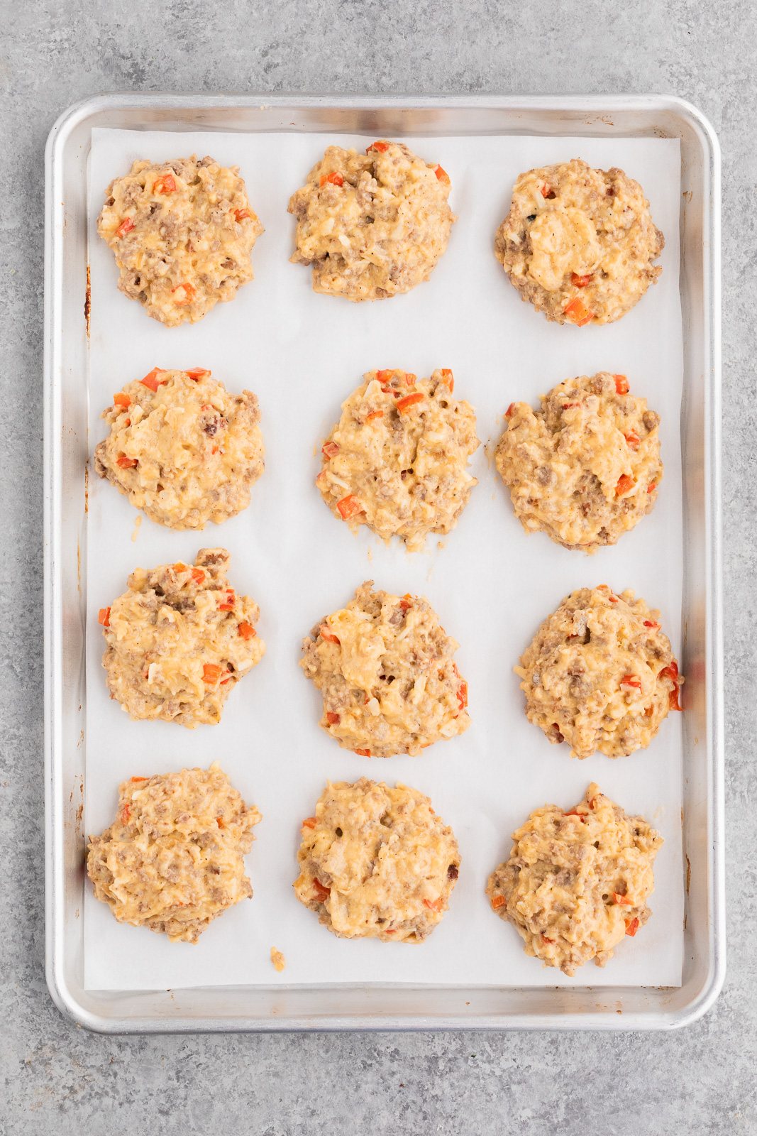 Scooping sausage egg biscuit dough onto a parchment-lined baking sheet before baking