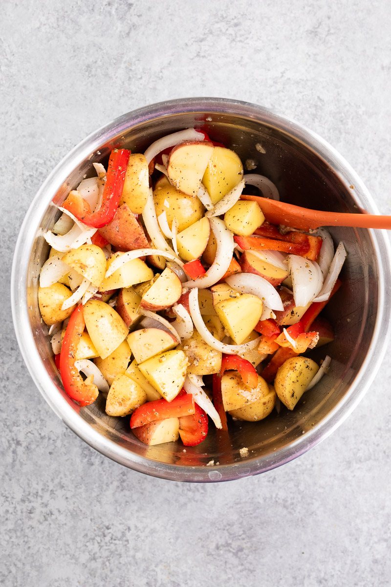 mixing sausage and vegetables with aromatics in a bowl