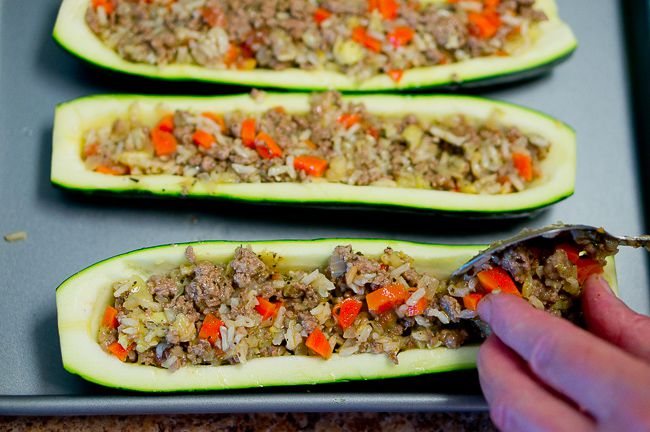 The filling being placed into the zucchini with a spoon