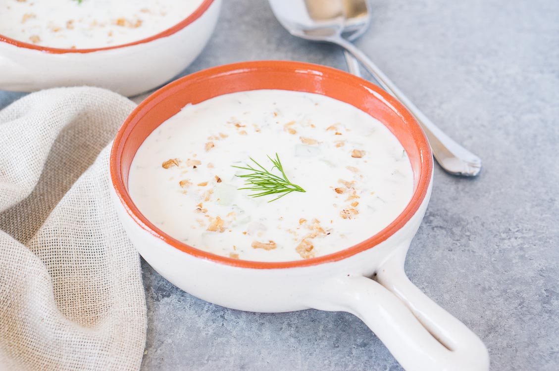 chilled cucumber yogurt soup with dill and walnuts in a clay bowl