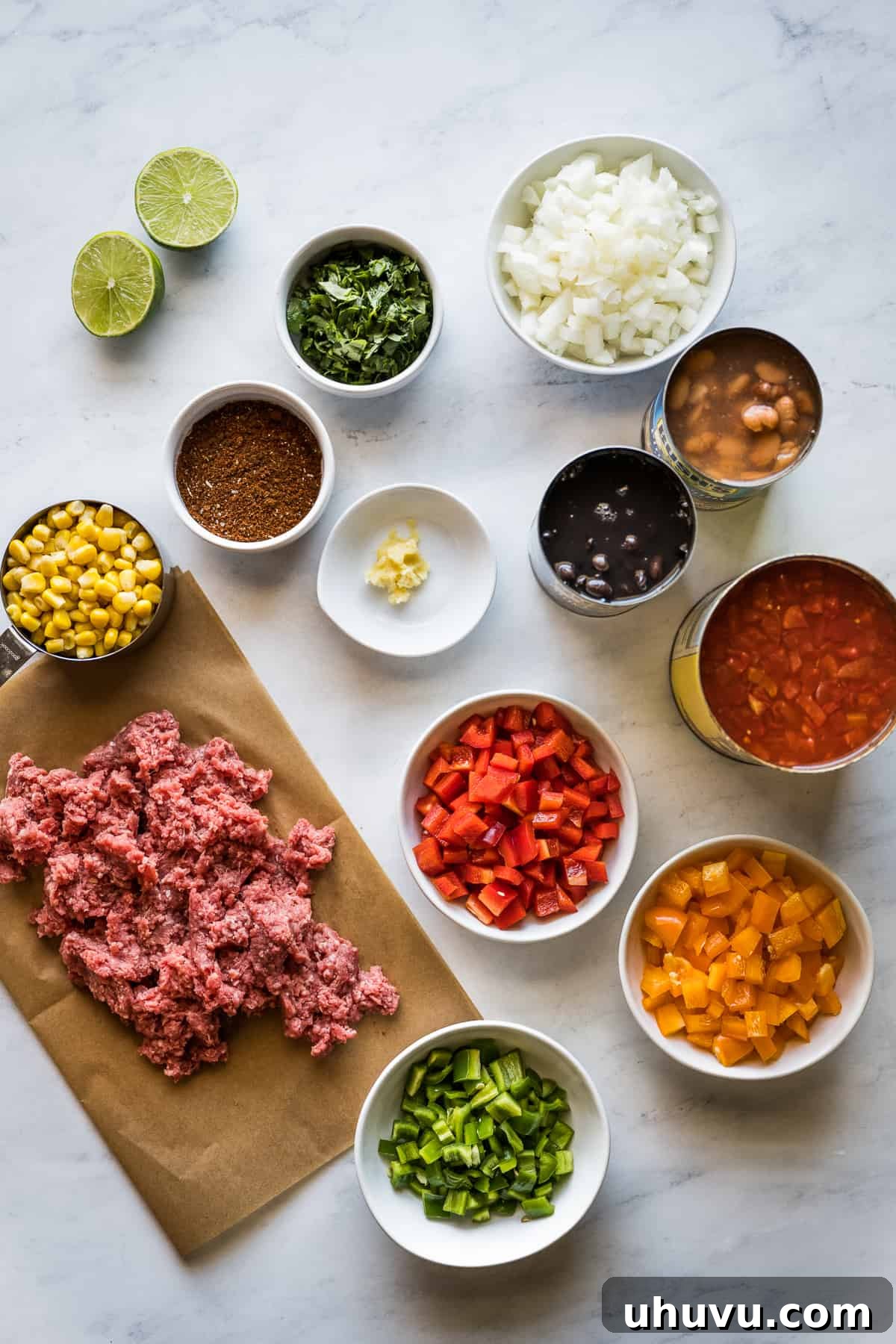 A colorful array of ingredients for Taco Soup laid out on a wooden board, including ground beef, bell peppers, onions, canned goods, and spices.