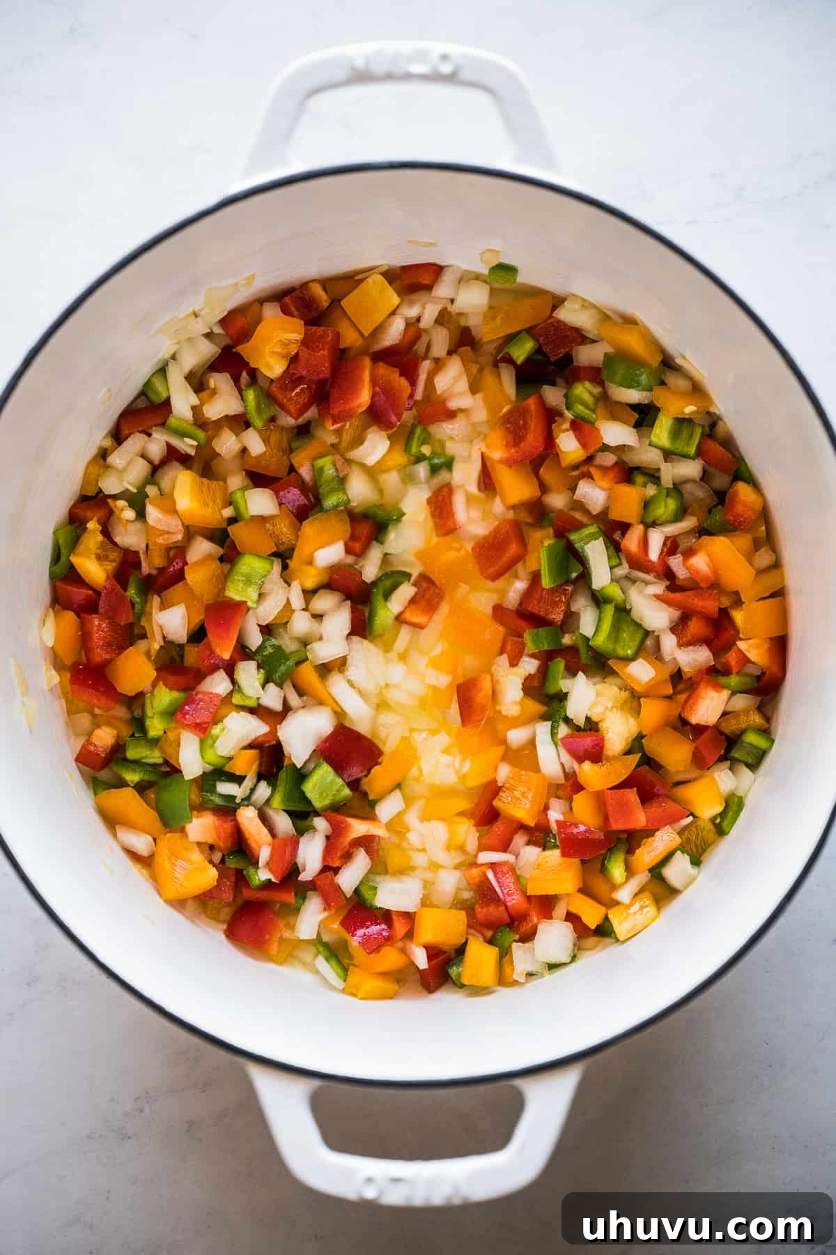 Bell peppers, onions, and garlic cooking in a large pot with olive oil.