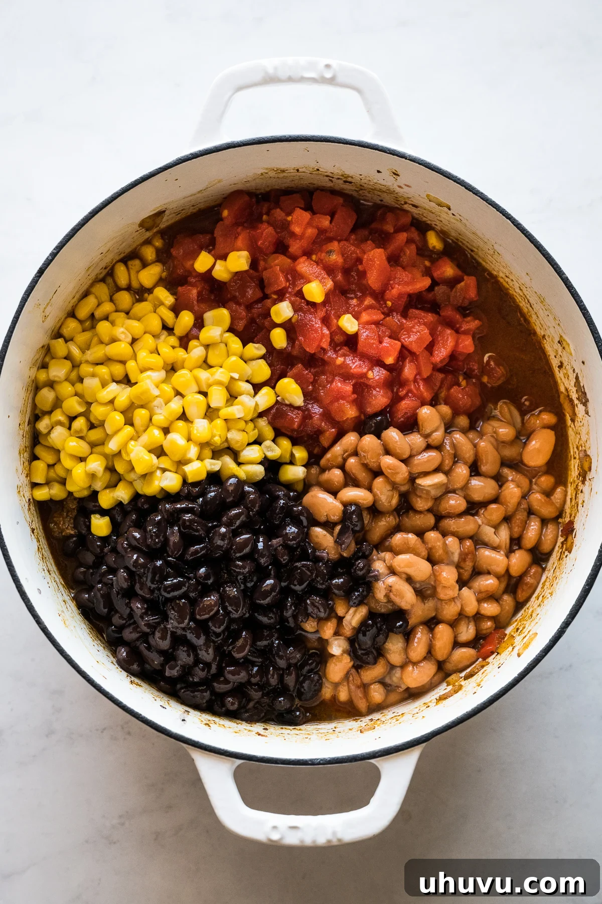 Corn, black beans, pinto beans, and diced tomatoes being added to the browned meat and vegetable mixture in a pot for taco soup.