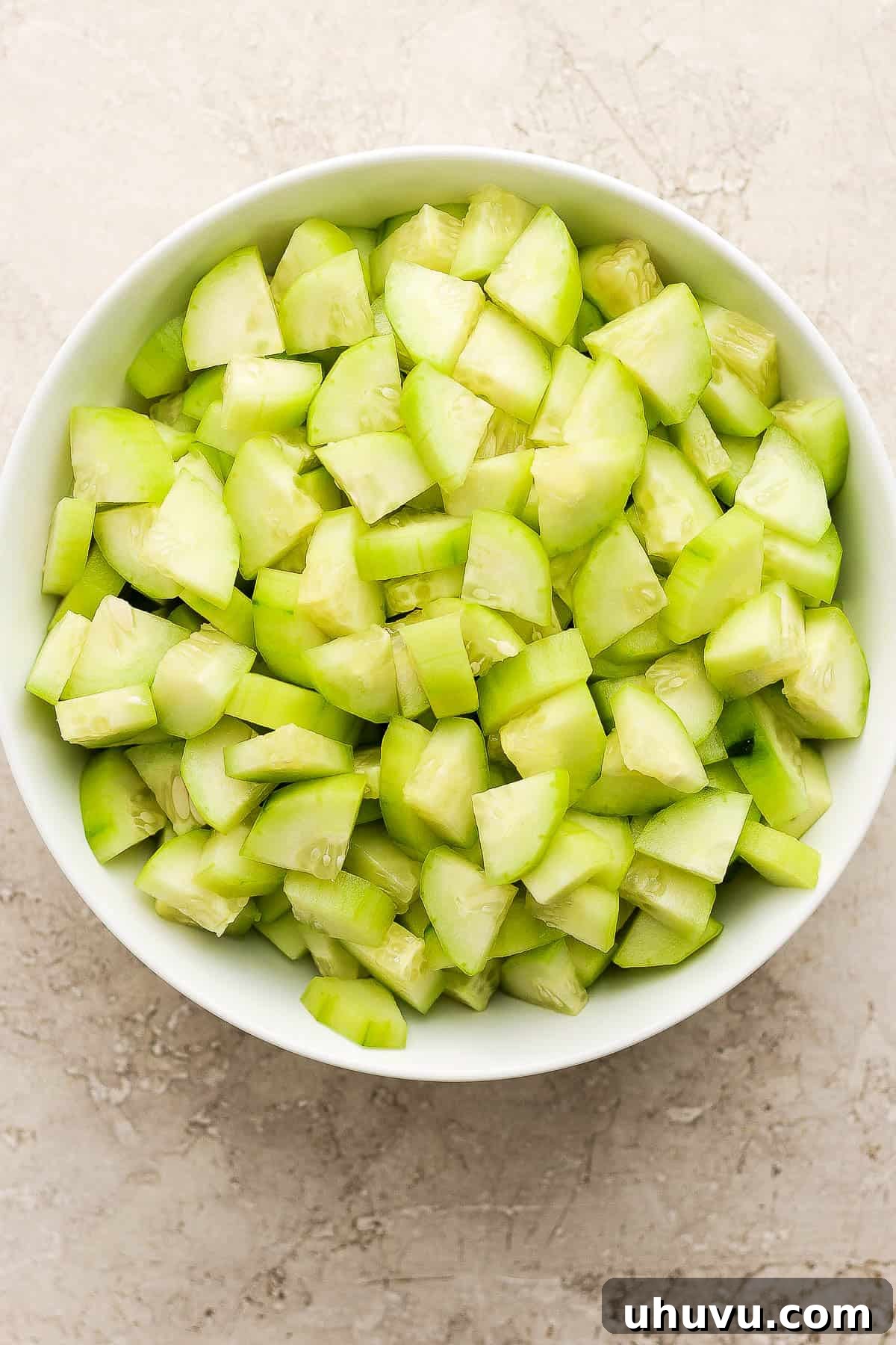 Neatly peeled and chopped cucumbers resting in a large clear bowl, ready for blending into Agua de Pepino.