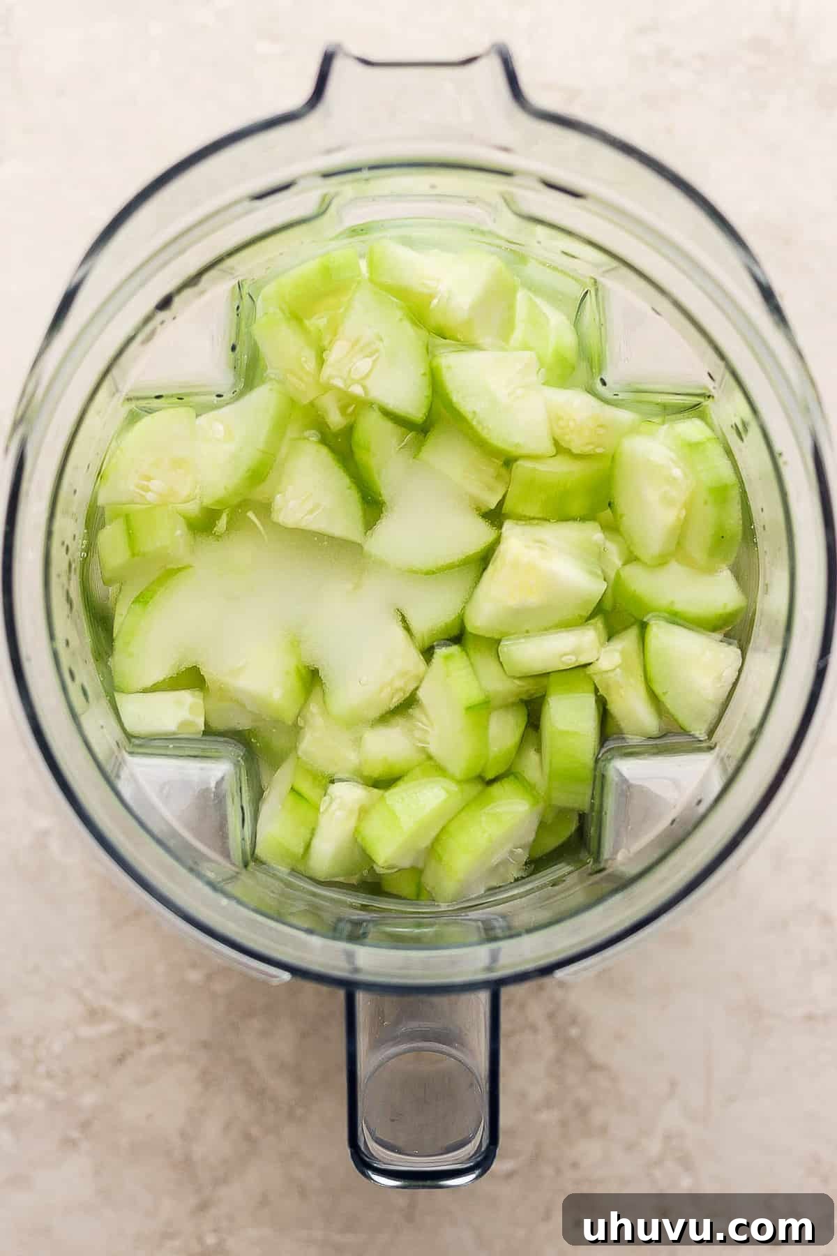 A blender filled with peeled cucumbers, water, and granulated sugar, ready to be processed into a refreshing drink.