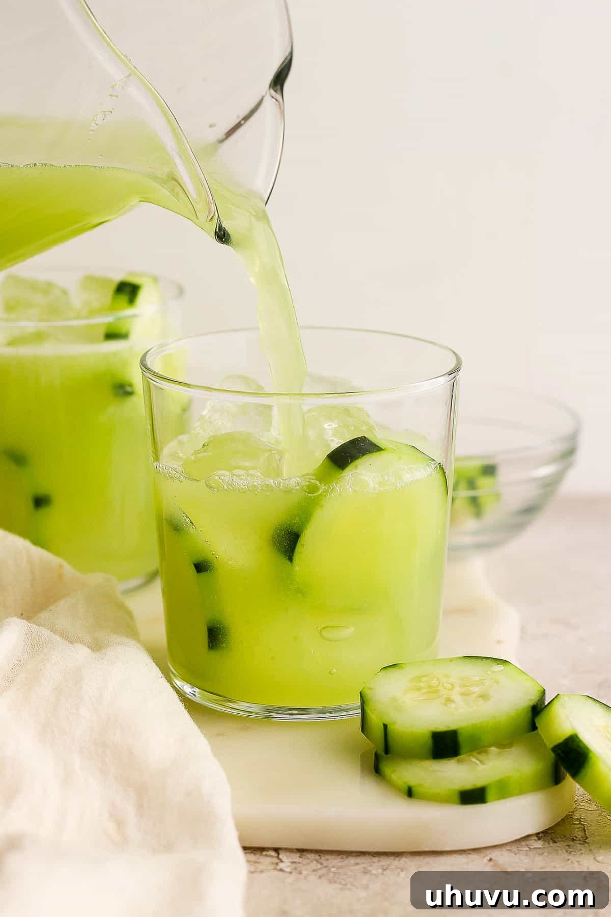 A stream of freshly made Agua de Pepino pouring into a glass filled with ice, ready to be savored.
