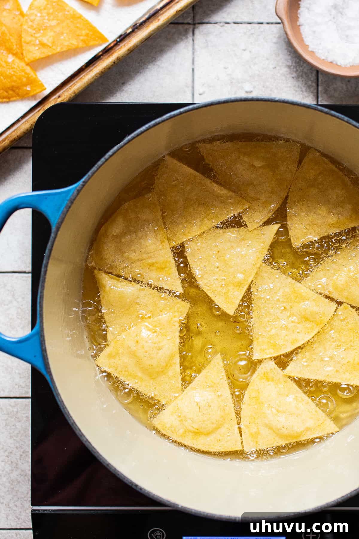 Golden Homemade Tortilla Chips 5 Corn tortilla triangles actively frying in hot oil in a pot, turning golden brown.