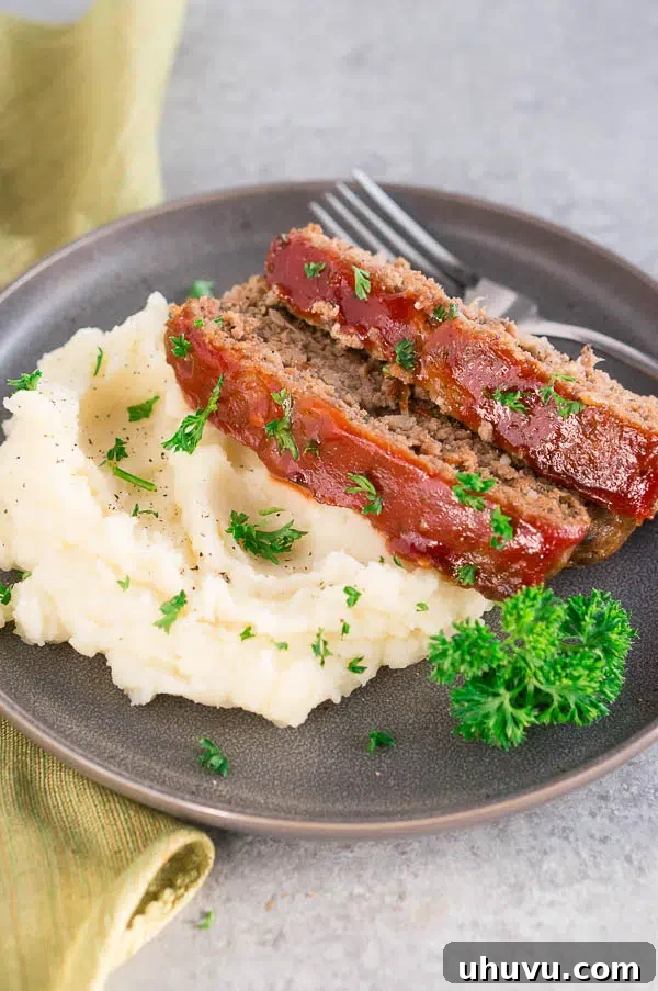 Slices of perfectly glazed meatloaf served over fluffy mashed potatoes, highlighting its rich, comforting appeal.