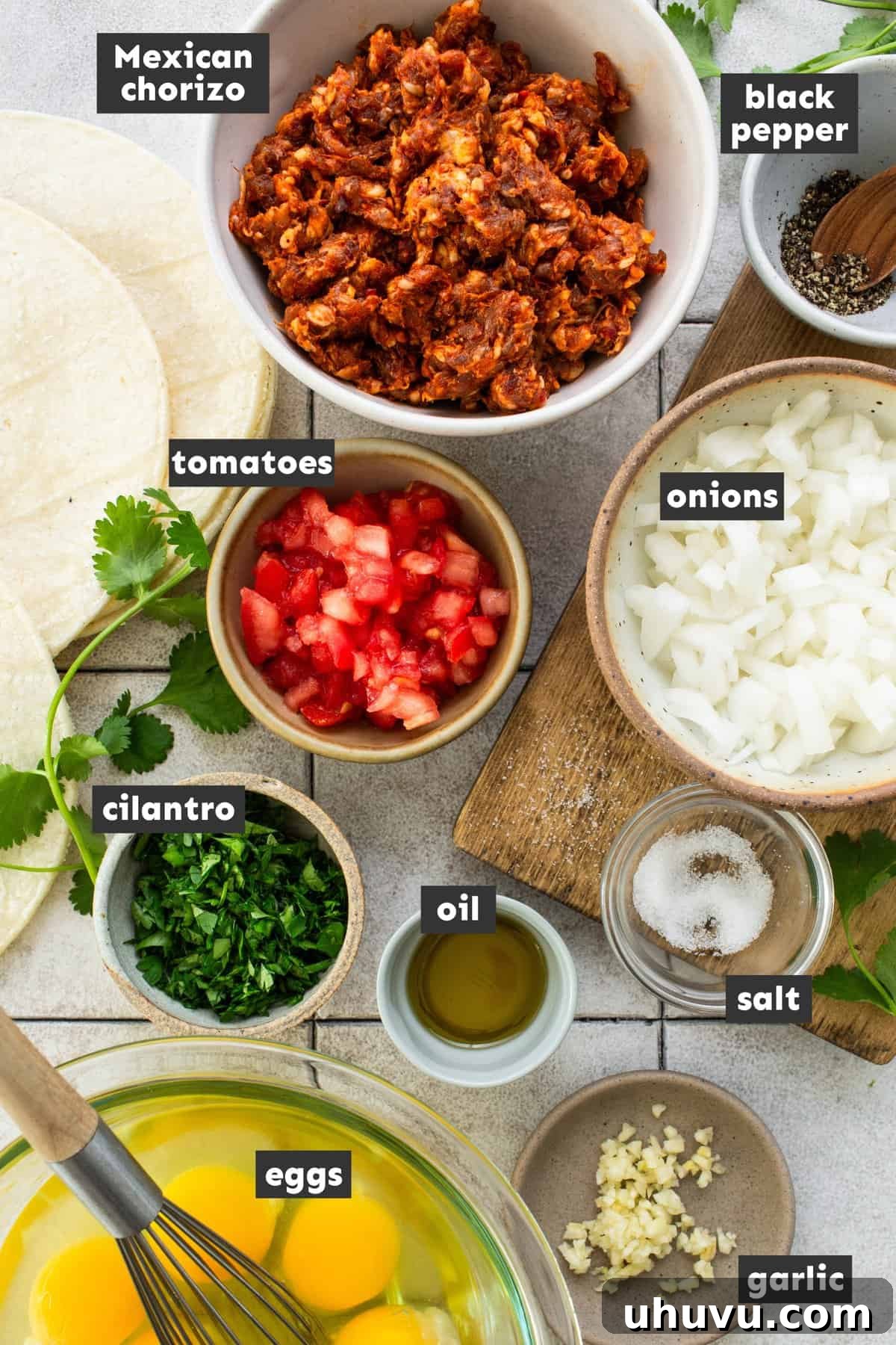 Fiery Chorizo Morning 3 A visually appealing flat lay of fresh ingredients laid out on a table, including raw Mexican chorizo, farm-fresh eggs, ripe tomatoes, a white onion, and garlic cloves, essential for making Chorizo and Eggs.