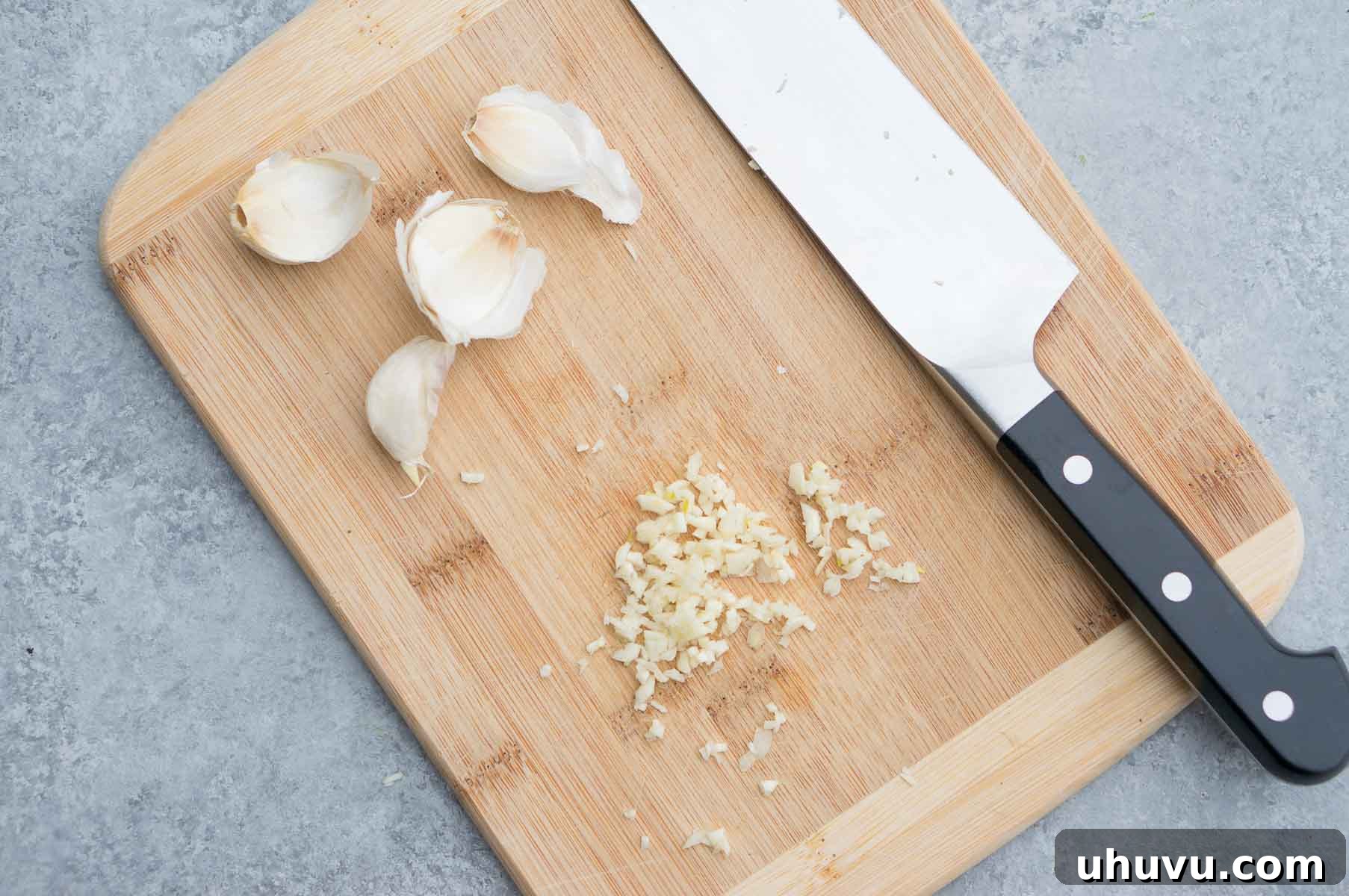 Master the Art of Cutting Garlic 3 Different kitchen tools for preparing garlic: a sharp chef's knife, a manual garlic press, and a Microplane grater shown on a cutting board