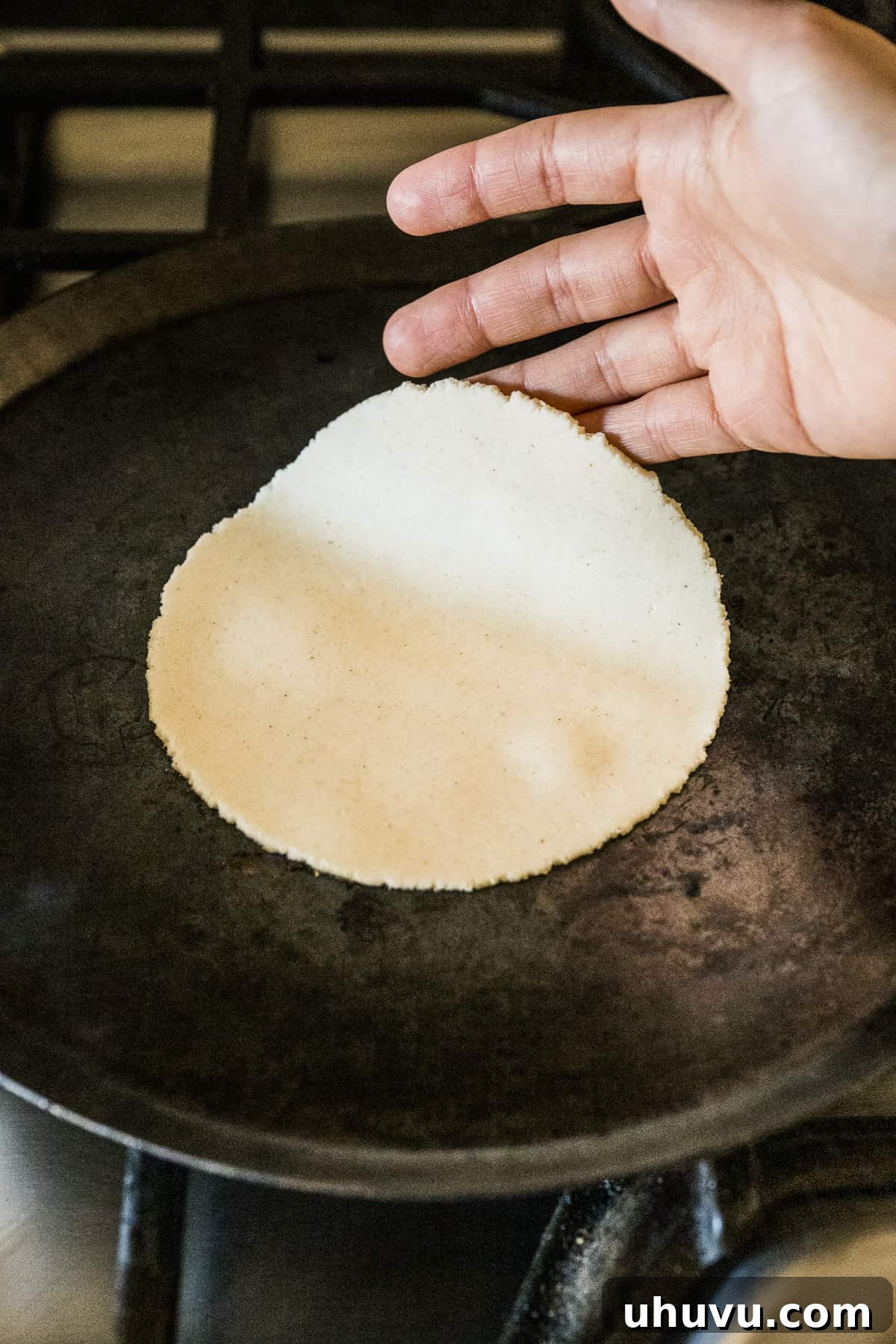 A corn tortilla cooking on a hot comal, beginning to develop light golden spots.
