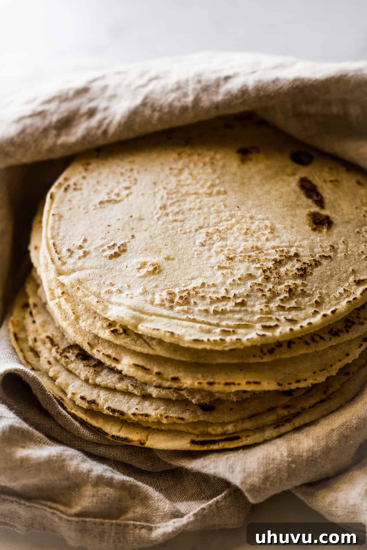 A inviting stack of perfectly cooked homemade corn tortillas, wrapped in a kitchen towel to keep them warm.