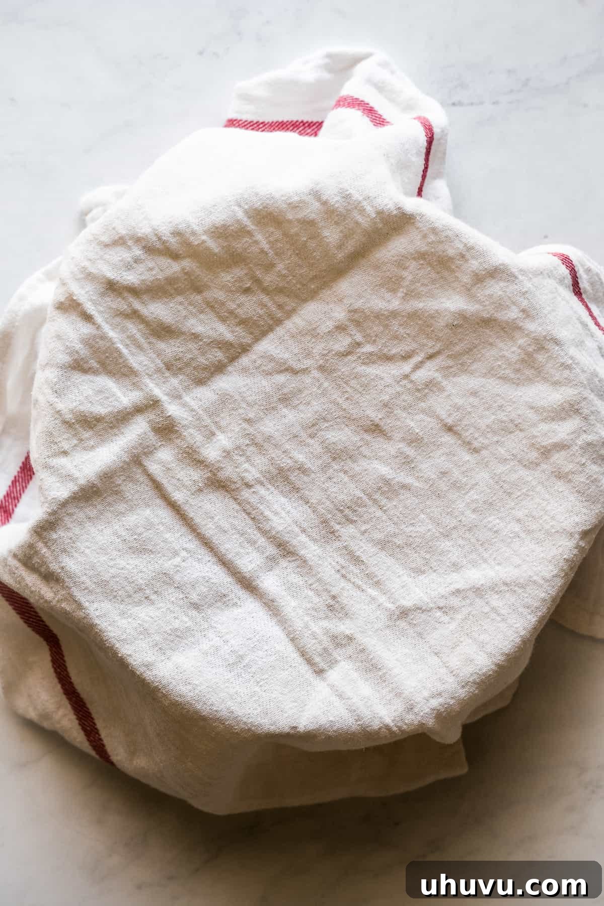 Masa harina dough balls being covered with a kitchen towel to prevent them from drying out before pressing.