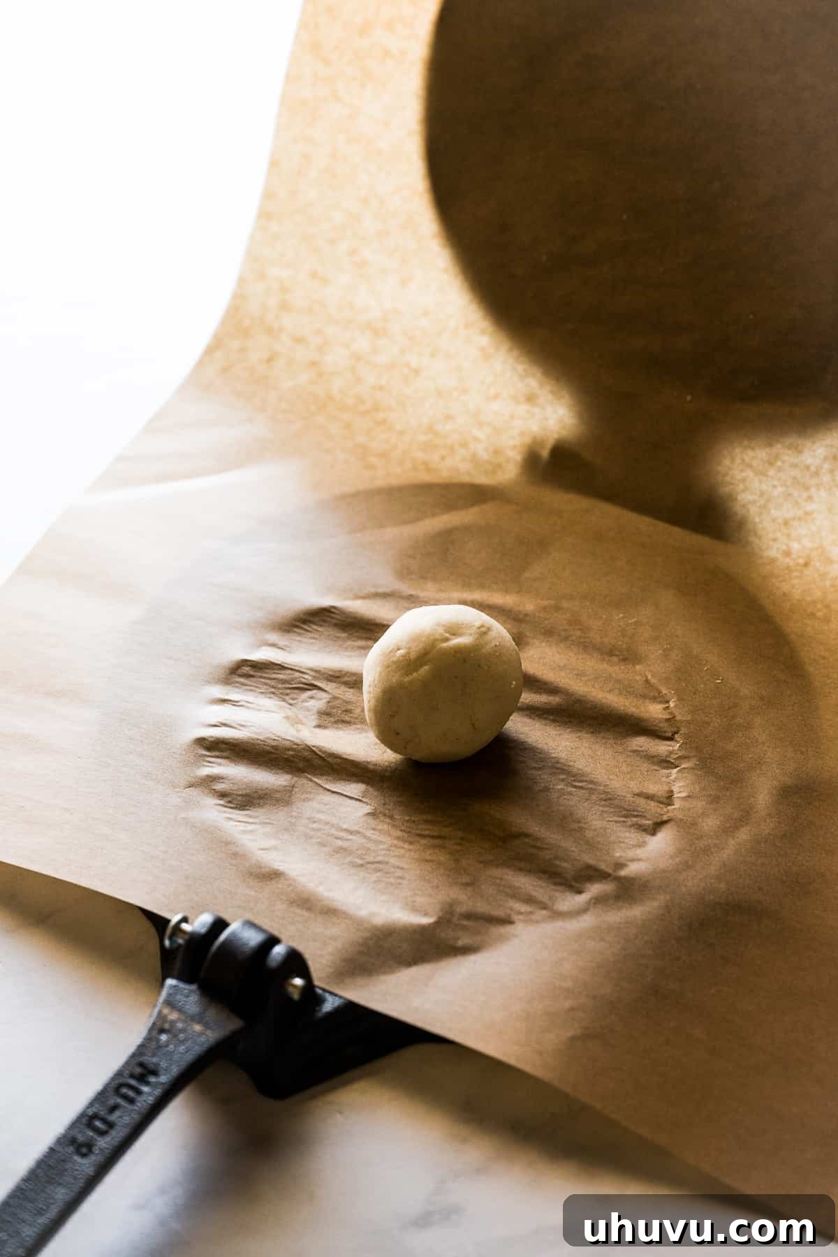 A perfectly portioned ball of masa harina dough placed on a lined tortilla press, ready to be flattened.
