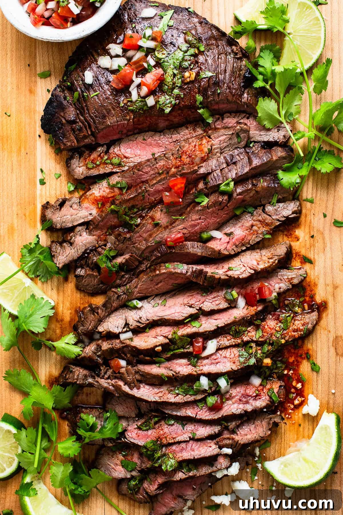 Perfect Grilled Carne Asada 7 Thinly sliced carne asada on a cutting board with some pico de gallo and chopped cilantro on top.