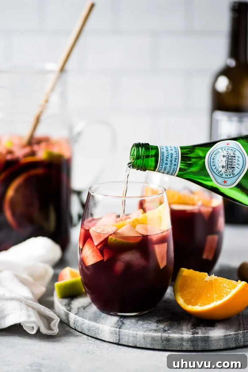 Sangria served in a glass, generously topped with colorful chunks of fresh fruit, including oranges and apples.