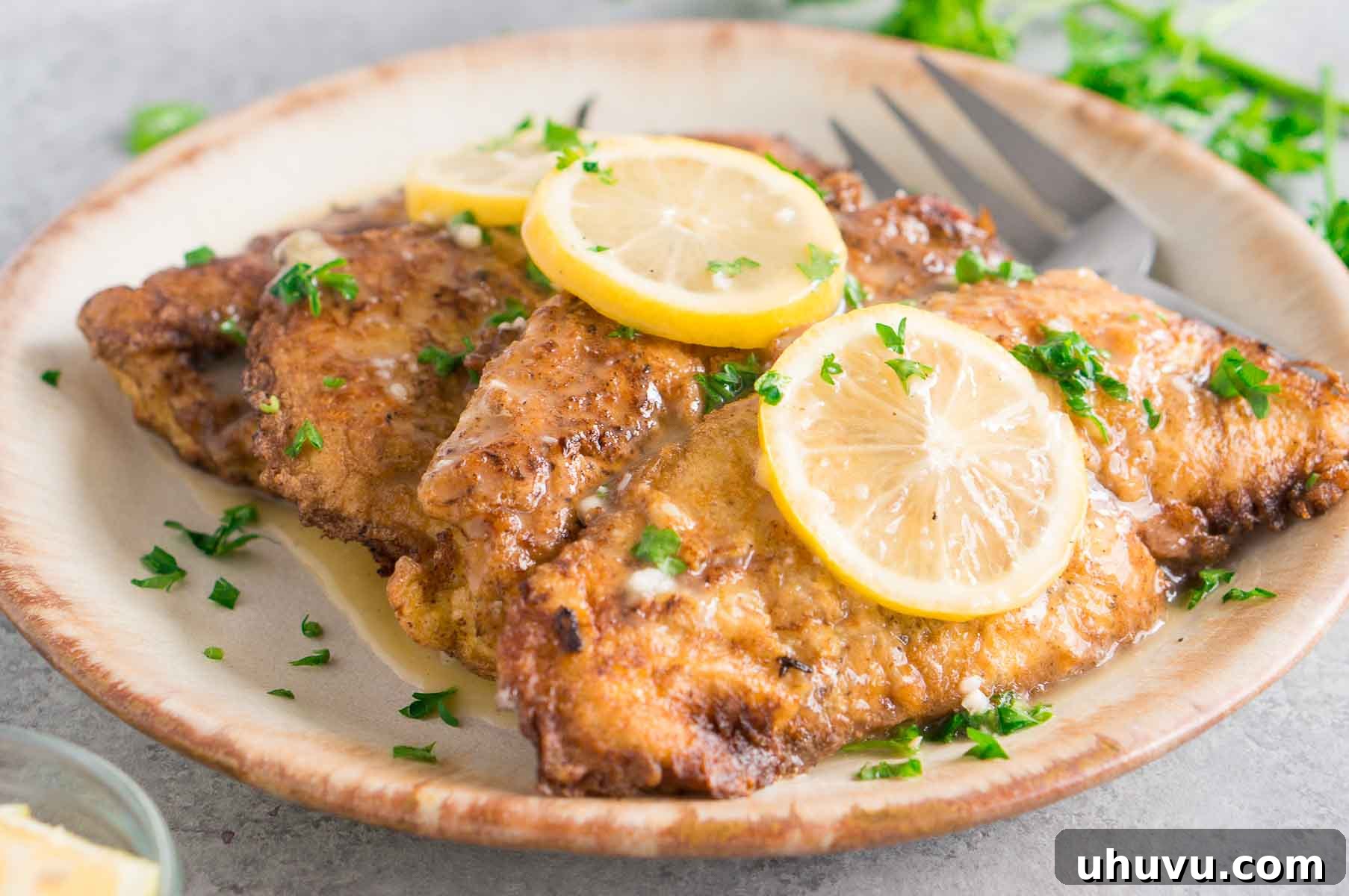 Close-up of golden-brown chicken cutlets bathed in lemon butter sauce, garnished with fresh herbs.