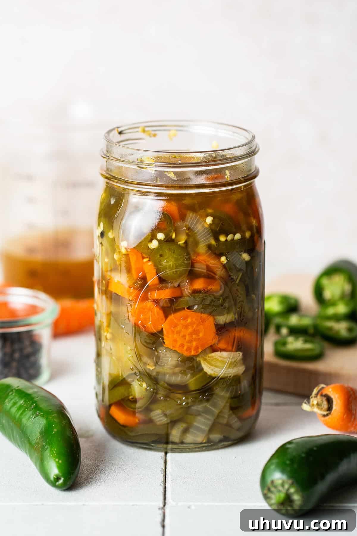 Zesty Pepper Bites 2 Pickled jalapenos in a jar ready to eat. A visually appealing jar filled with bright green jalapeño slices, alongside carrots and onions, preserved in a clear, flavorful brine.