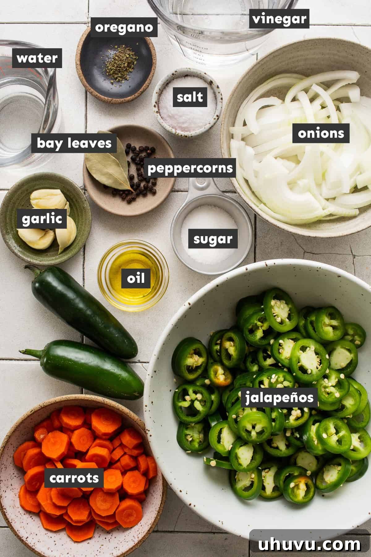 Zesty Pepper Bites 3 Ingredients for making pickled jalapeños on a table. Fresh jalapeños, carrots, onions, garlic, and various spices are laid out, ready for preparation.