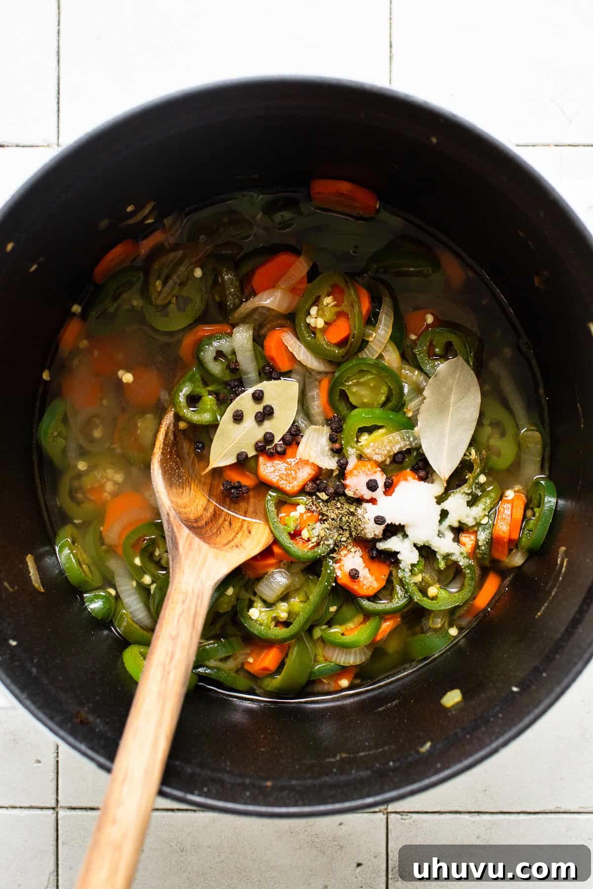 Zesty Pepper Bites 5 Jalapeños, onions, and carrots being pickled in a pot with lime juice, bay leaves, black peppercorns, salt, and oregano. The brine is bubbling gently around the colorful vegetables, infusing them with flavor.