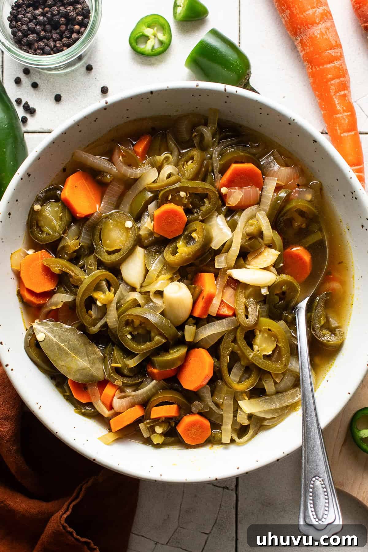 Zesty Pepper Bites 7 A bowl of pickled jalapeños Mexican escabeche style with carrots, onions, and garlic on a table. The vibrant mix of pickled vegetables is artfully arranged, ready to be served.