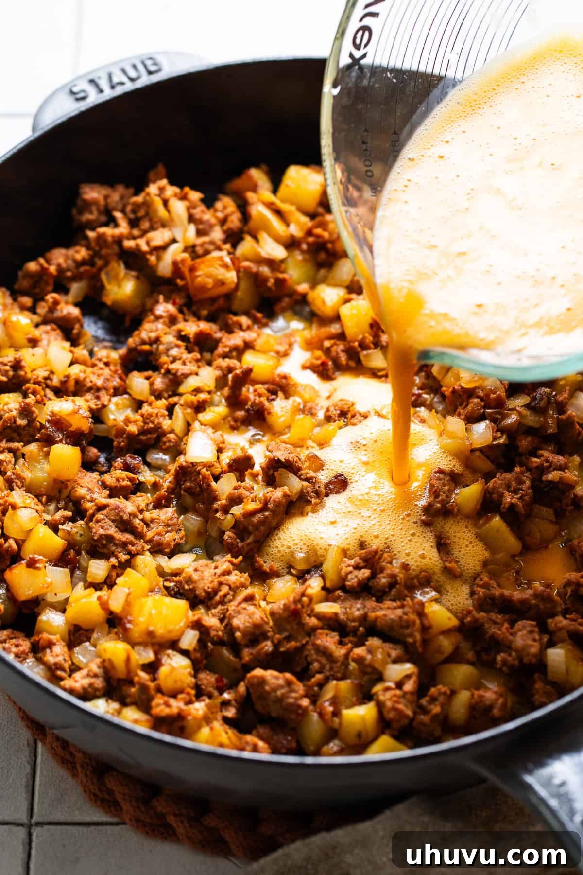 Morning Taco Bliss 5 Beaten eggs being poured into the skillet with a mixture of cooked potatoes, onions, and chorizo, ready to be gently scrambled.